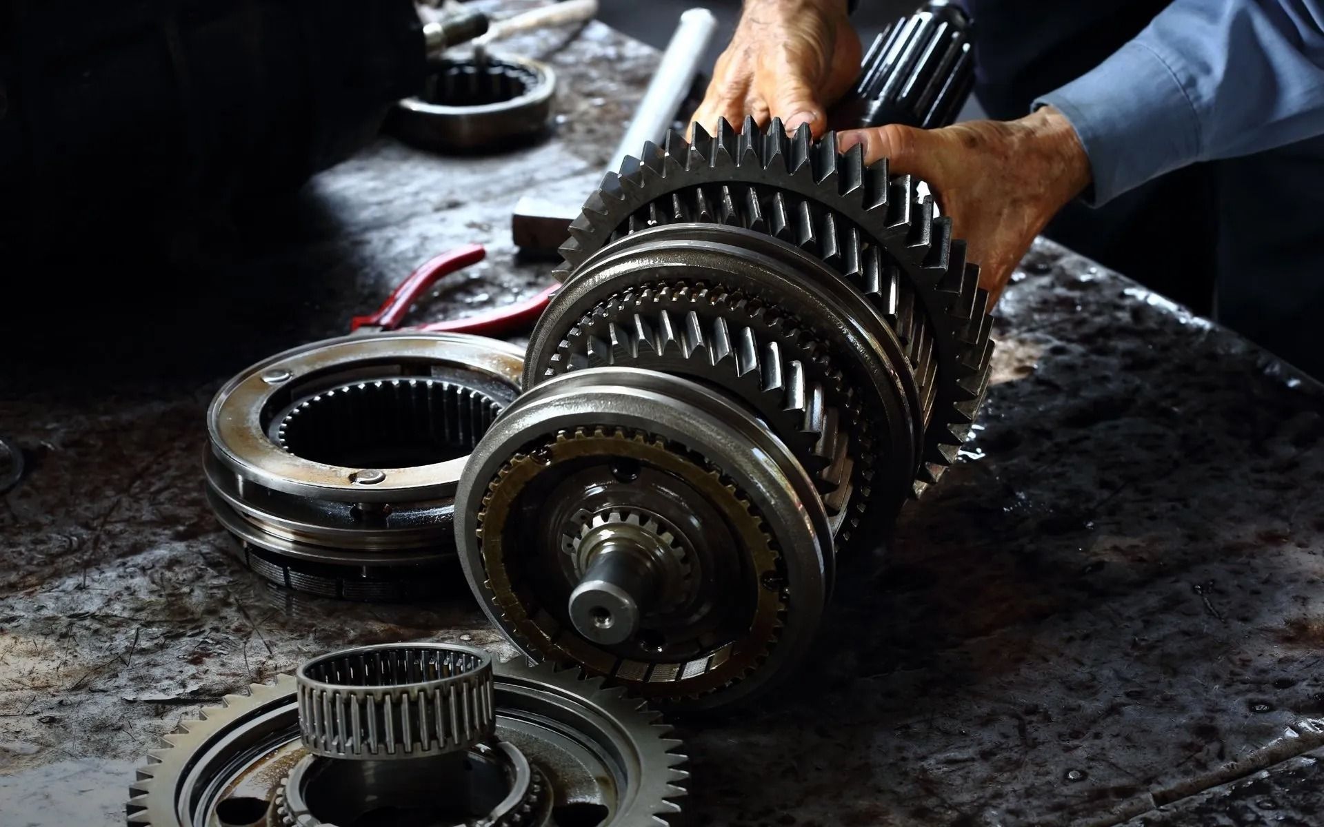 A mechanic's hands holding a disassembled transmission with gears on a workbench.