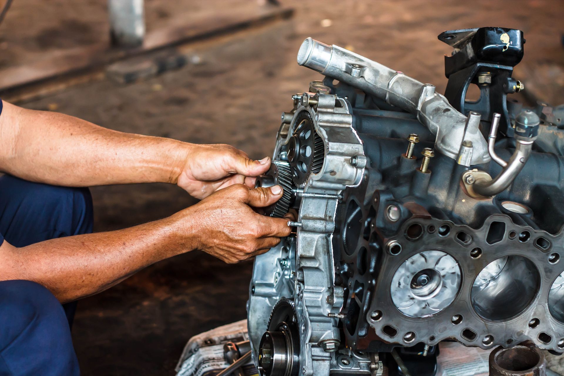 Mechanic working on an engine, attaching a part. Workshop setting with visible engine components.