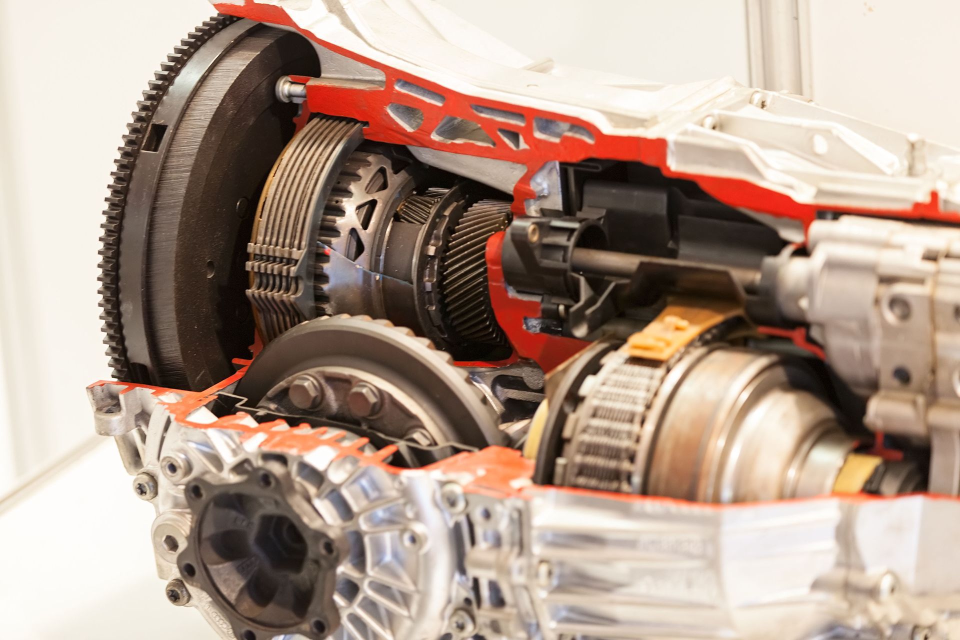 Cutaway view of a car transmission showing gears, shafts, and internal components in a red-highlighted metal casing.
