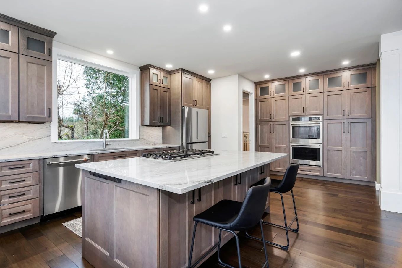 Modern kitchen with dark hardwood flooring, gray shaker cabinets, and marble counters