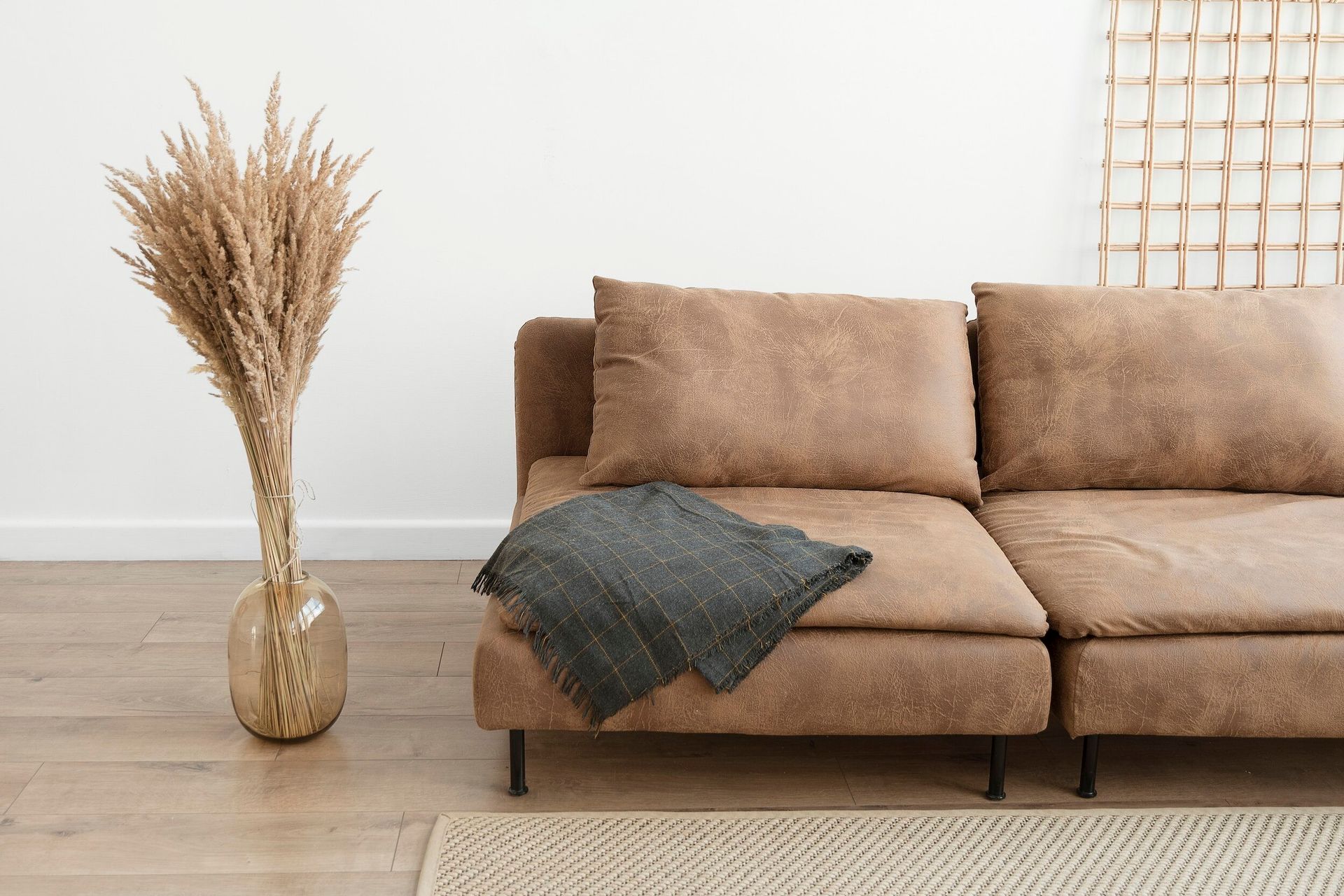 A living room with a brown couch and a vase of dried grass.