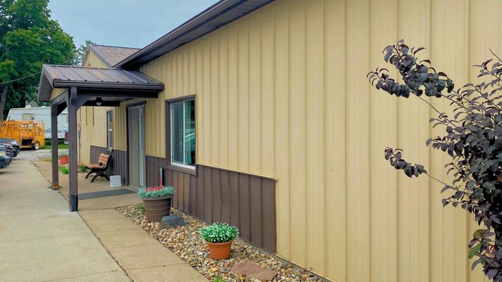 A yellow and brown building with a porch and flowers in front of it.