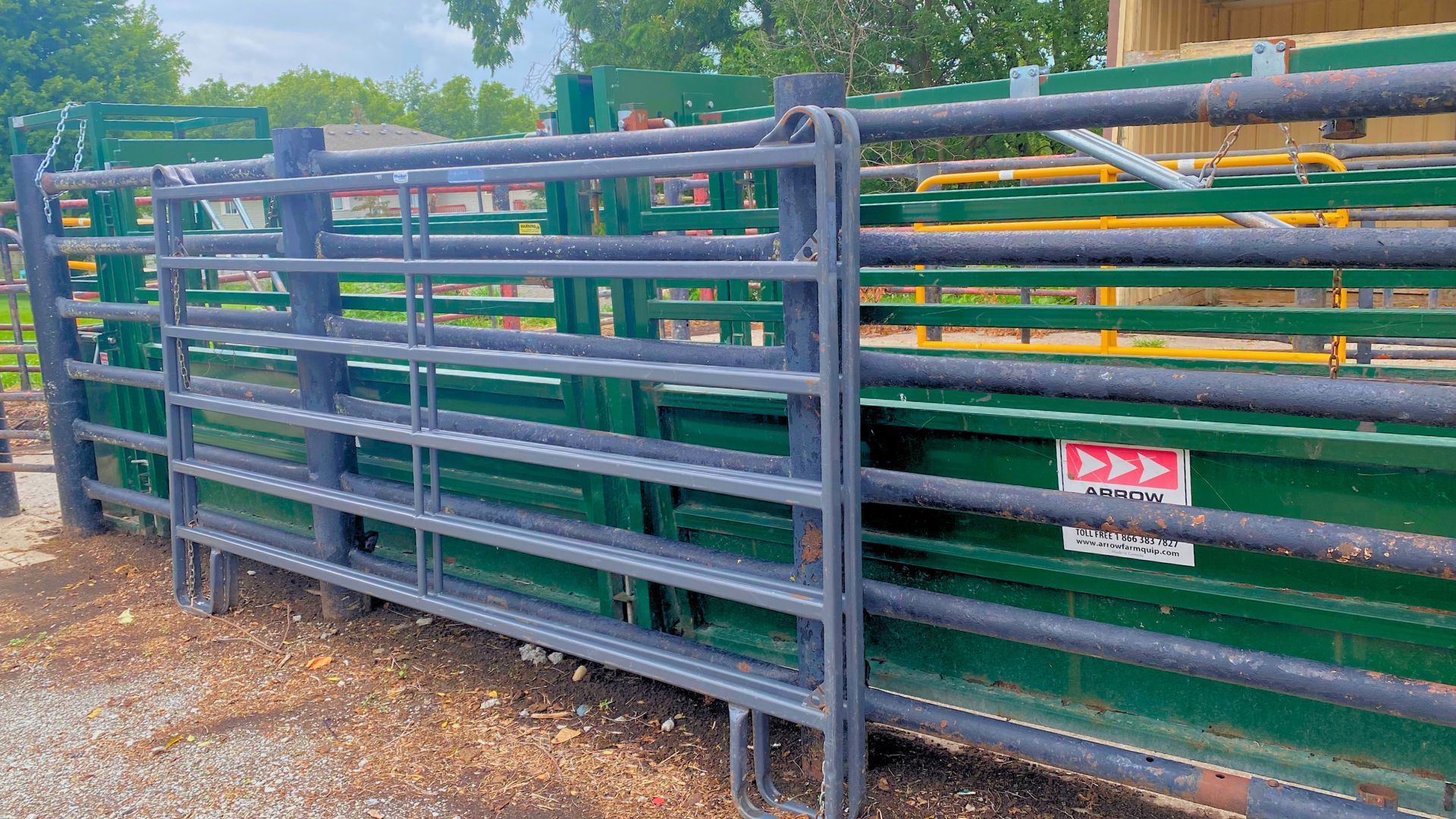 A green and black fence with a sign on it is sitting on top of a gravel road.