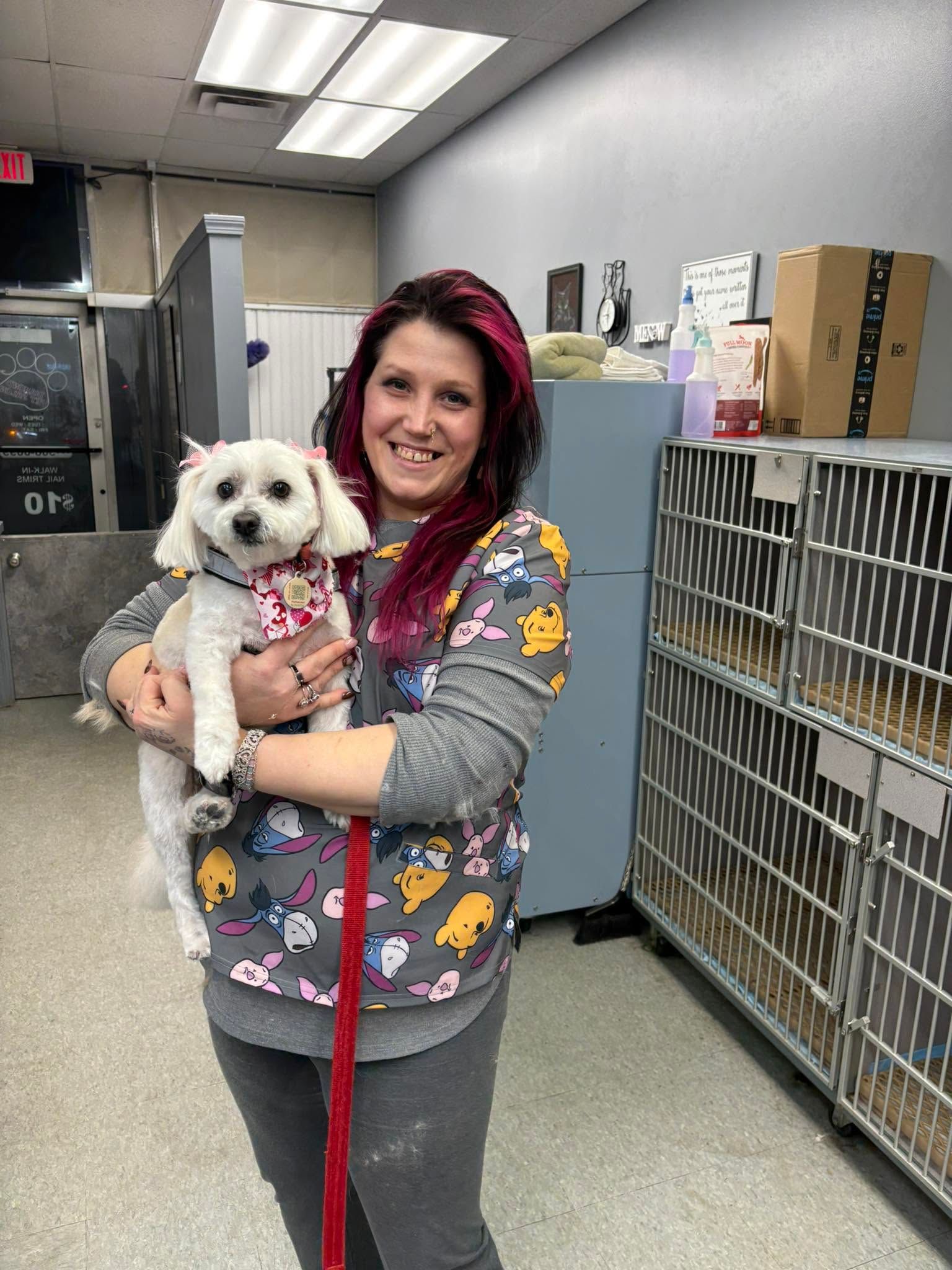 Smiling woman holding a small white dog on a red leash in a kennel hallway