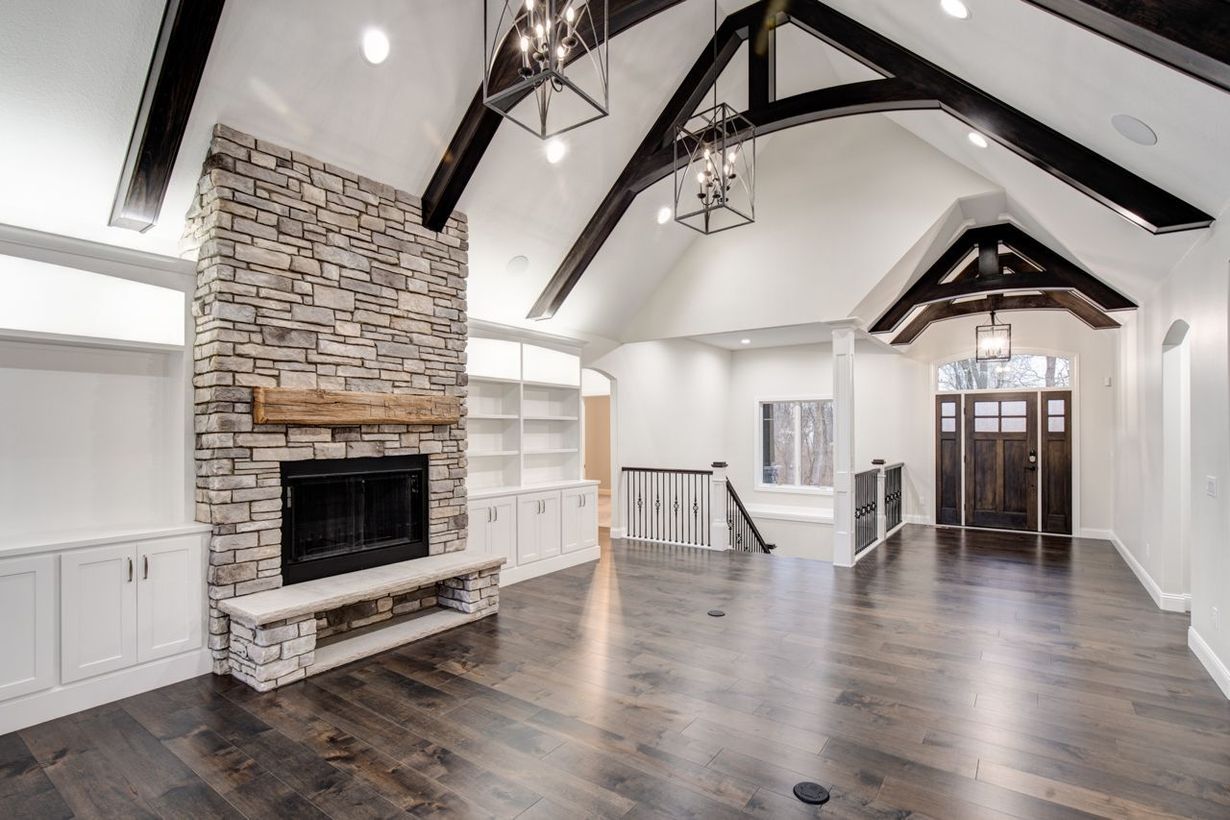 Spacious living room with stone fireplace, dark wood floors, white walls, and exposed beams.