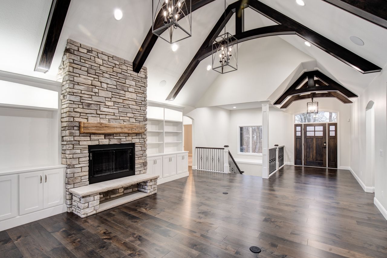 Spacious living room with stone fireplace, dark wood floors, white walls, and exposed beams.