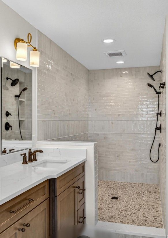 Bathroom with walk-in shower, pebble floor, and white subway tile walls. Vanity with wood cabinets and gold sconces.