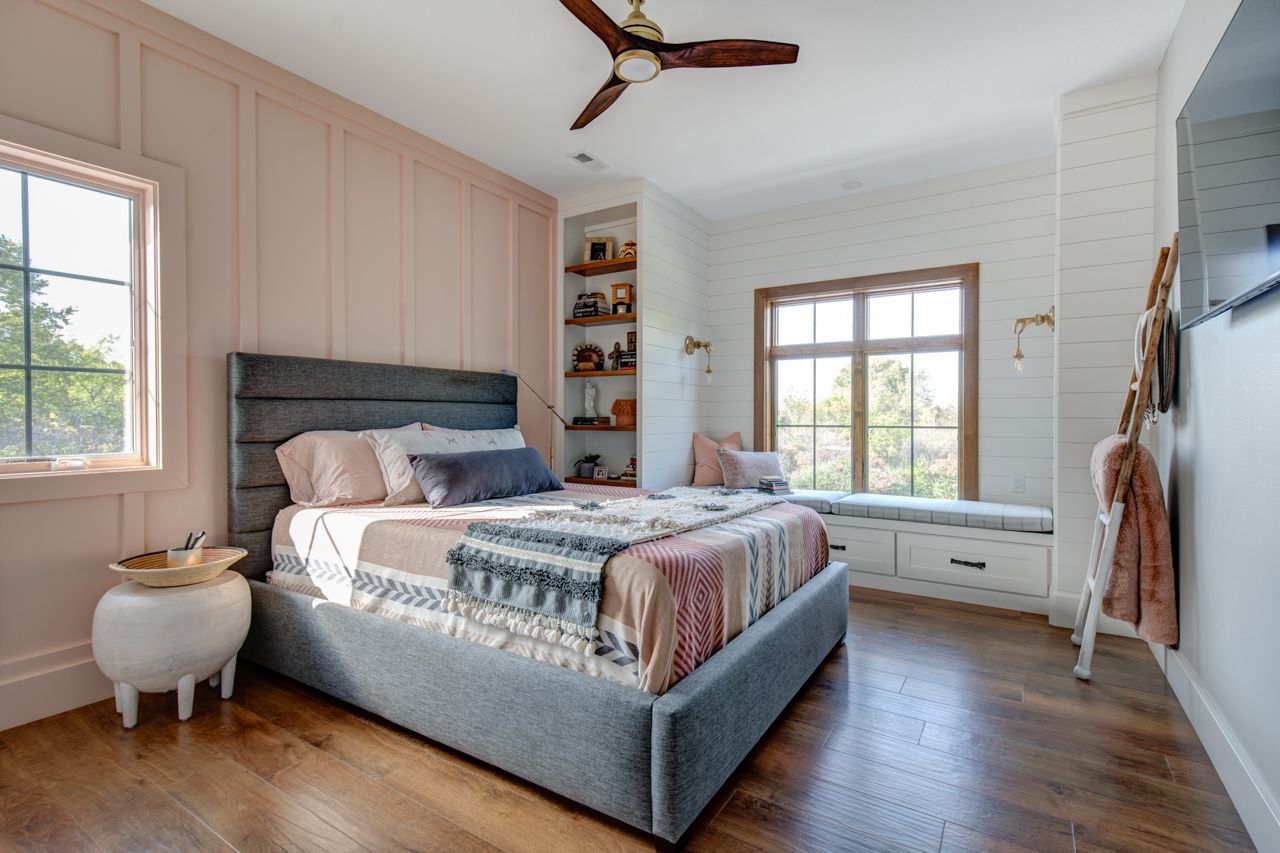 Bedroom with pink wall paneling, gray bed, window seat, and wooden floors.