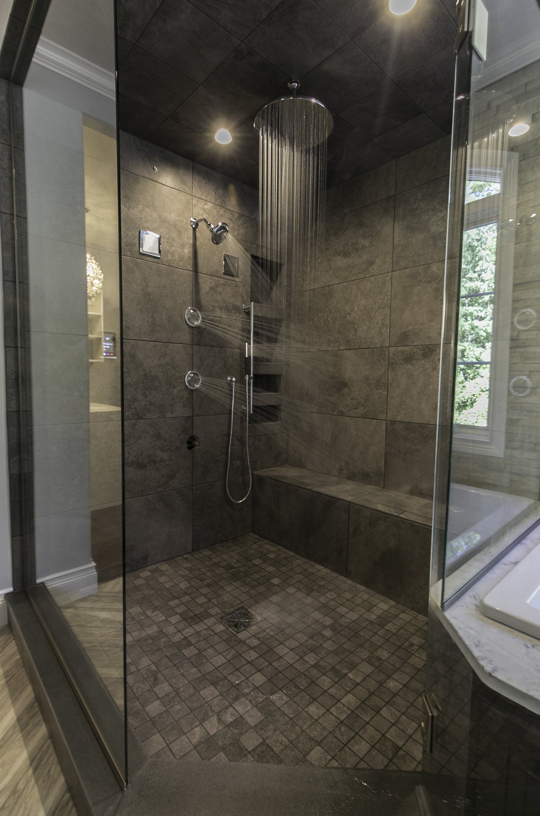 Modern shower with stone tile walls, rainfall showerhead, glass enclosure, and built-in bench.