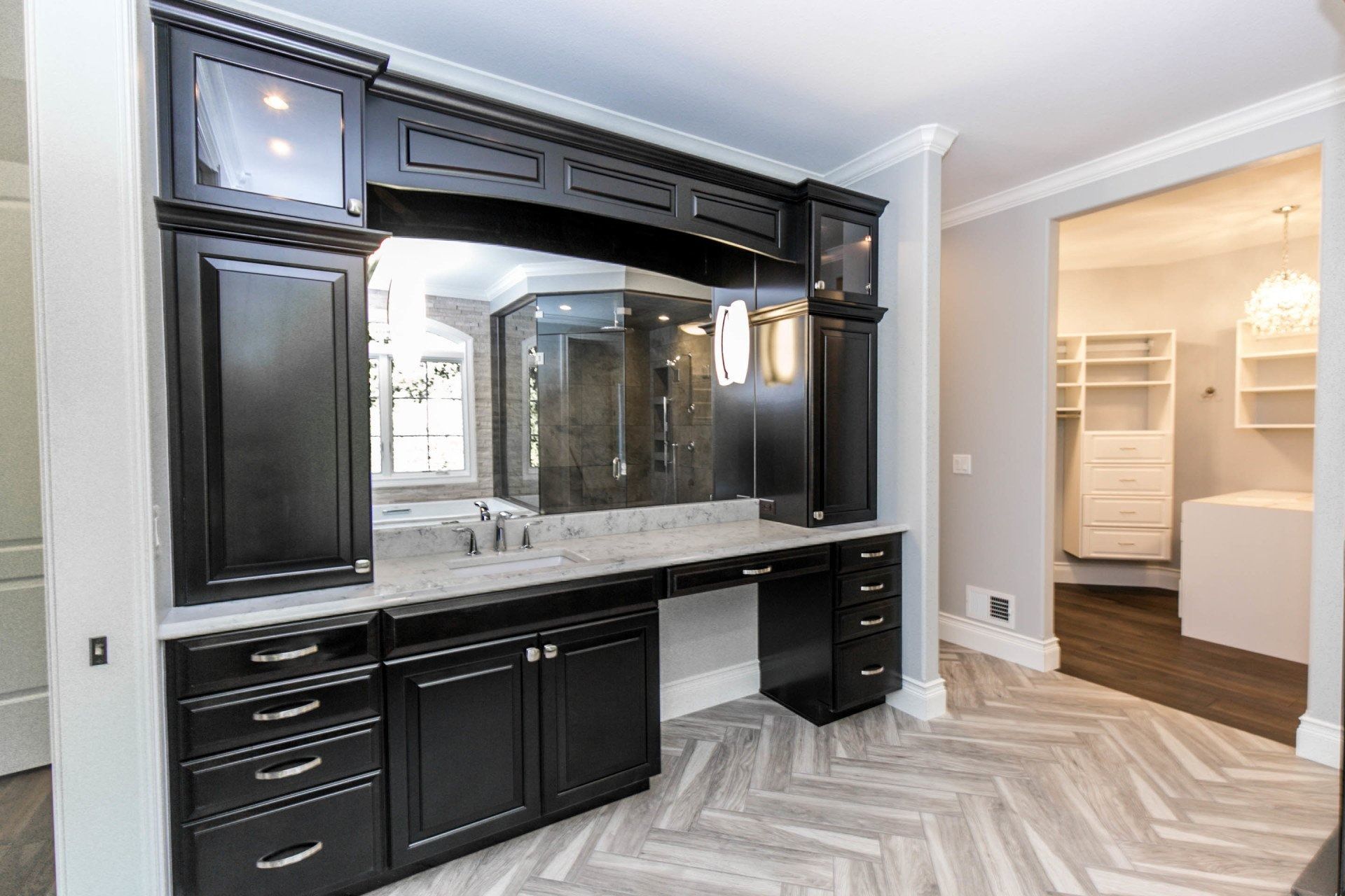 Black vanity with mirror and cabinets, countertop, drawers in a room with wood floors.