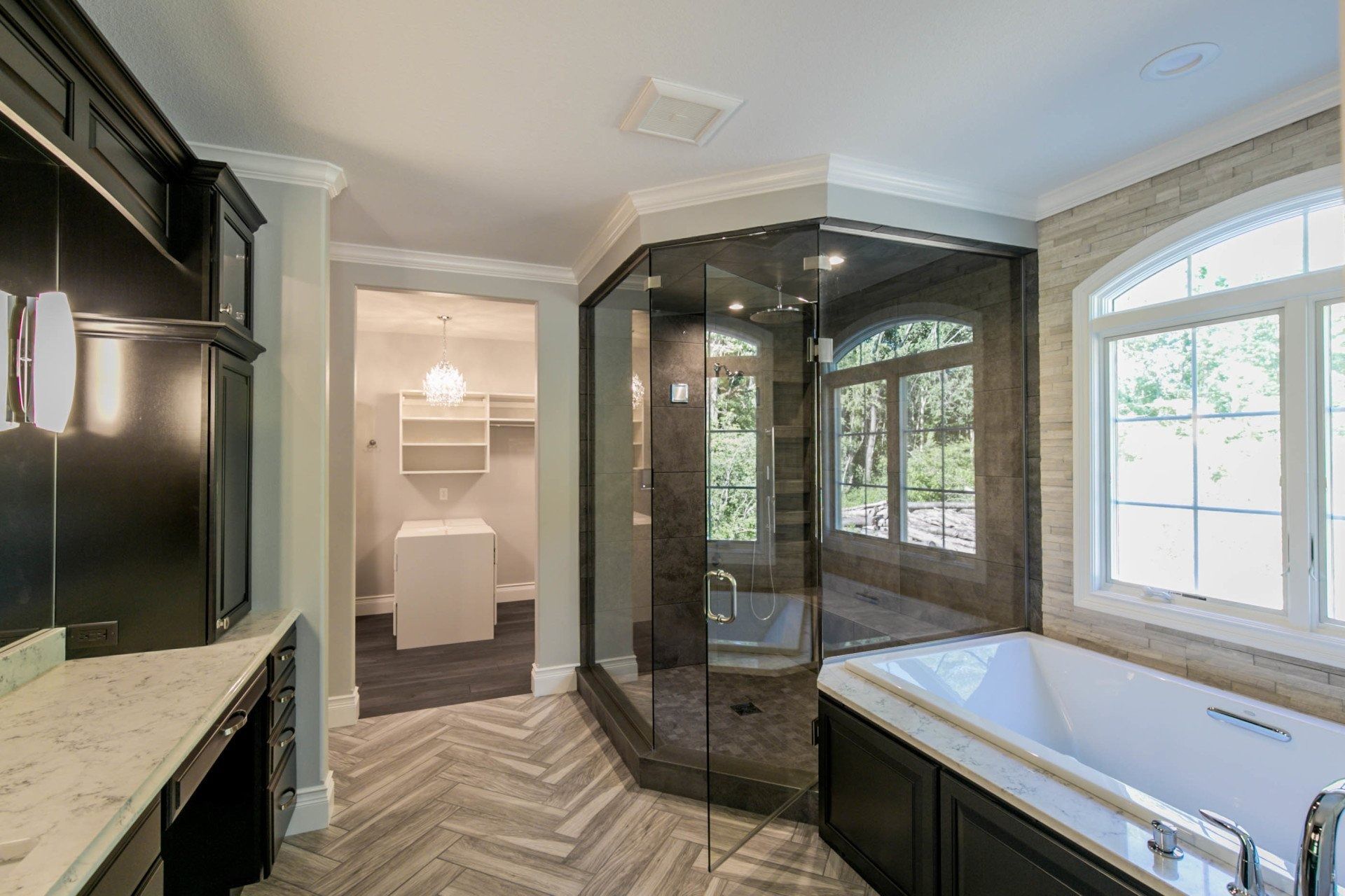 Bathroom with walk-in shower, soaking tub, vanity, and walk-in closet. Grey and black color scheme with natural light.