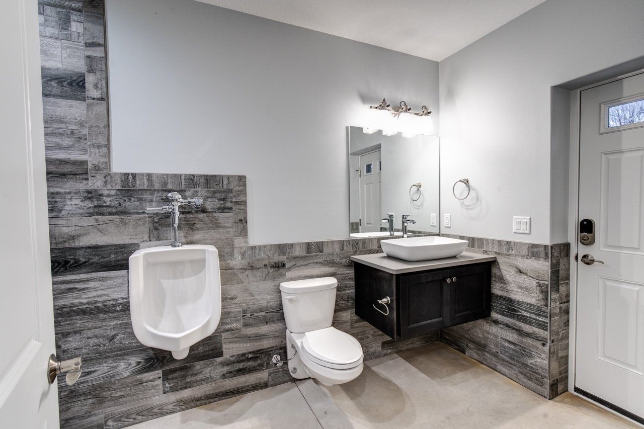 Bathroom with a urinal, toilet, and sink. Walls have gray wood-look tile. White door.