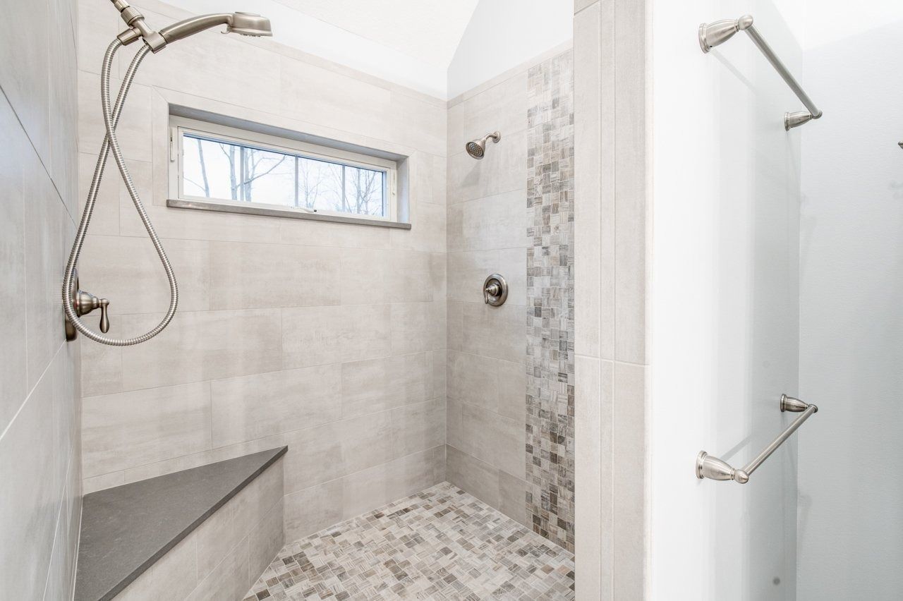 Bathroom shower with gray and white tile, shower bench, and window.