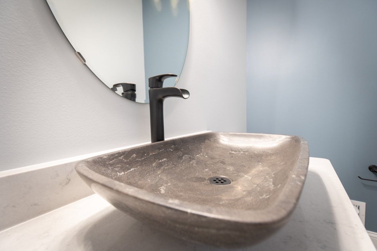 A gray stone vessel sink on a white countertop with a black faucet, set against a pale blue wall.