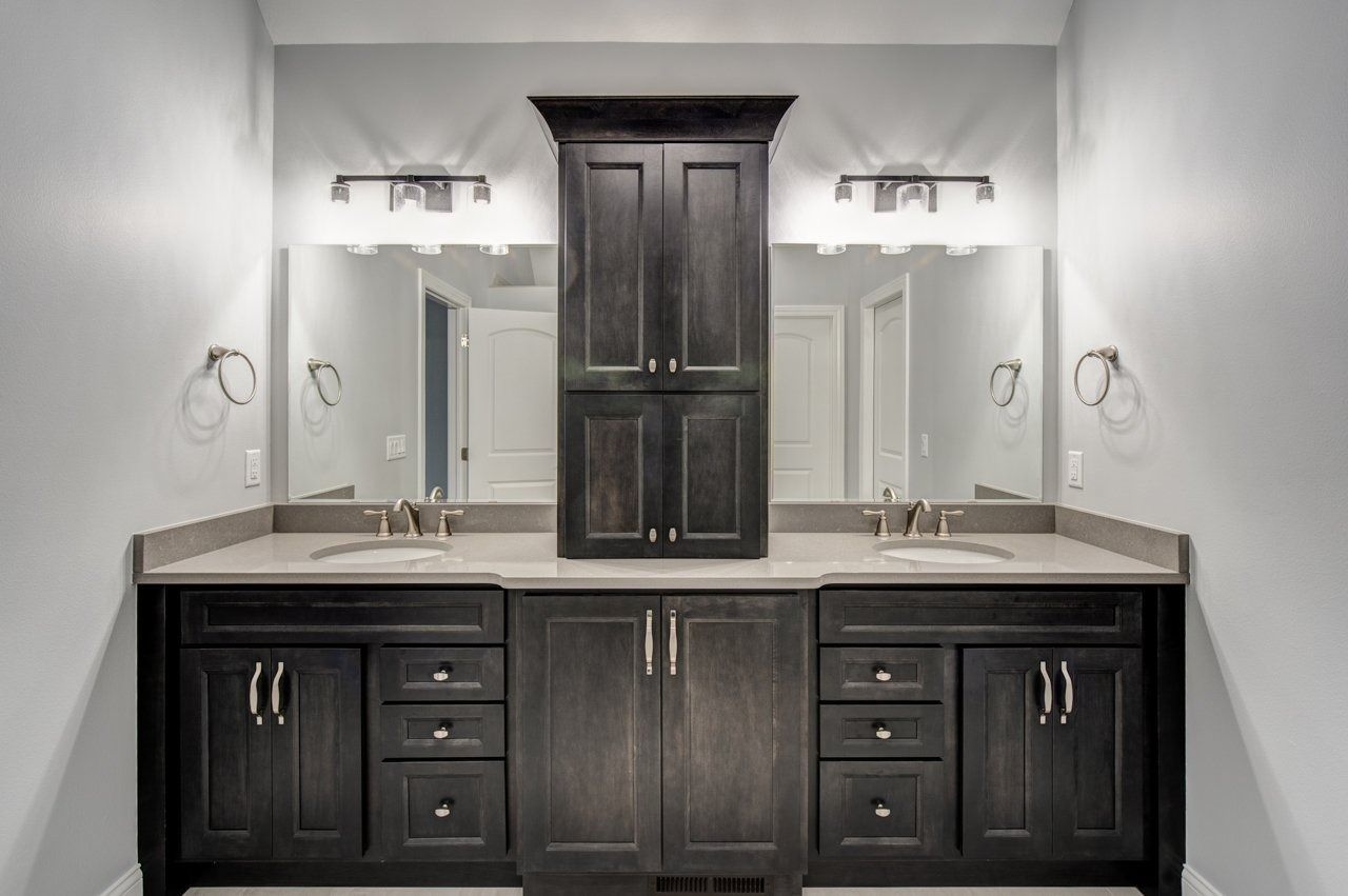 Bathroom with dark wood cabinetry, double vanity, mirrors, and center storage cabinet.