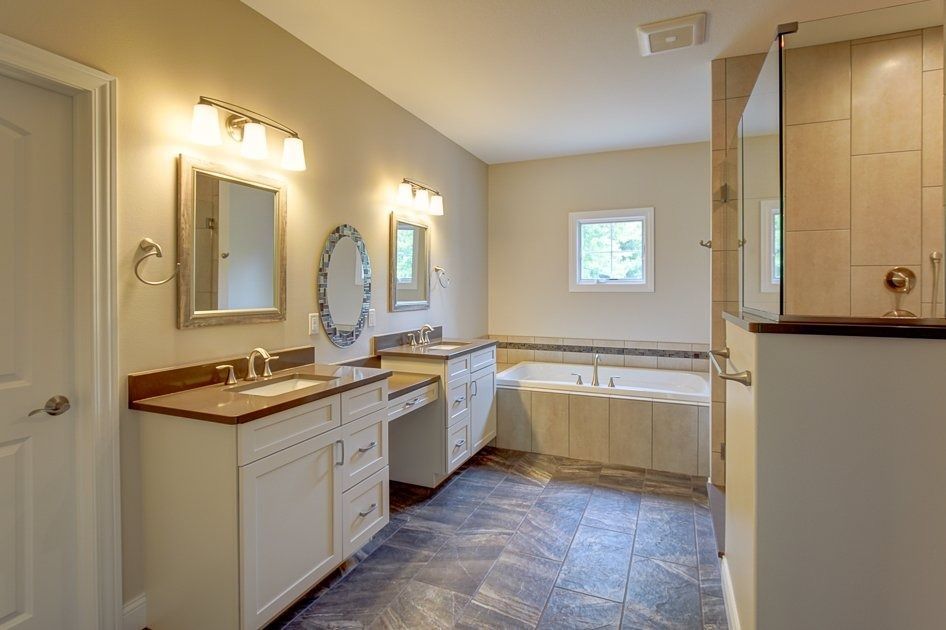 Spacious bathroom with two vanities, a bathtub, a shower, and dark blue tile flooring.