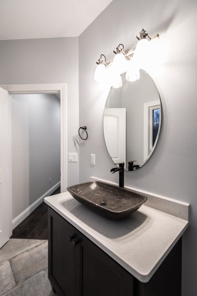 Bathroom with oval mirror, vessel sink, black faucet, and dark wood vanity; gray walls, white countertop.