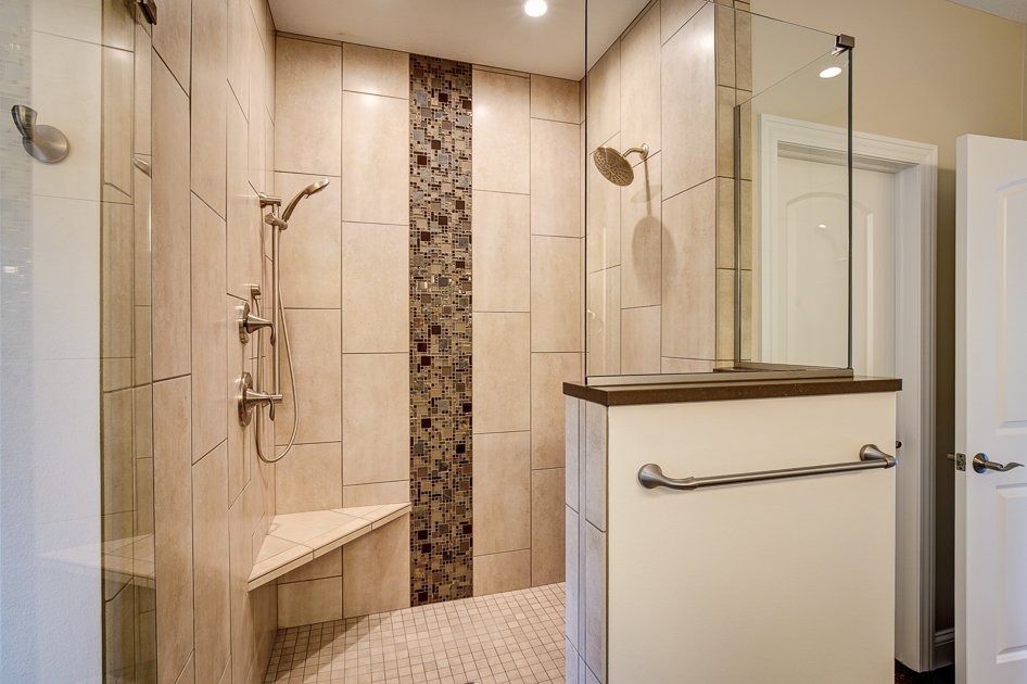 Spacious walk-in shower with beige tile, glass door, corner seat, and decorative dark tile stripe.