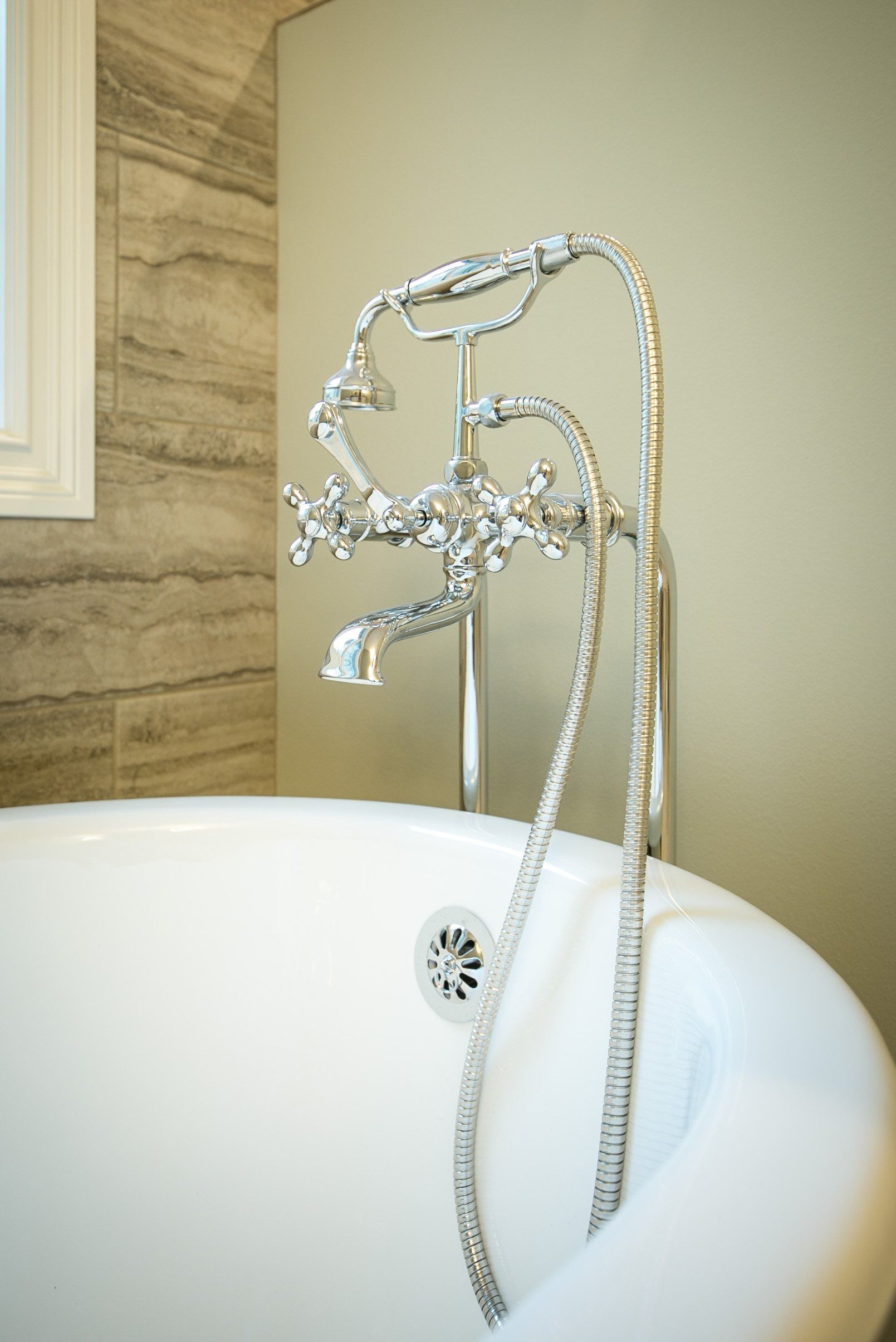 Chrome faucet and showerhead over a white, oval bathtub. Gray tile wall in background.