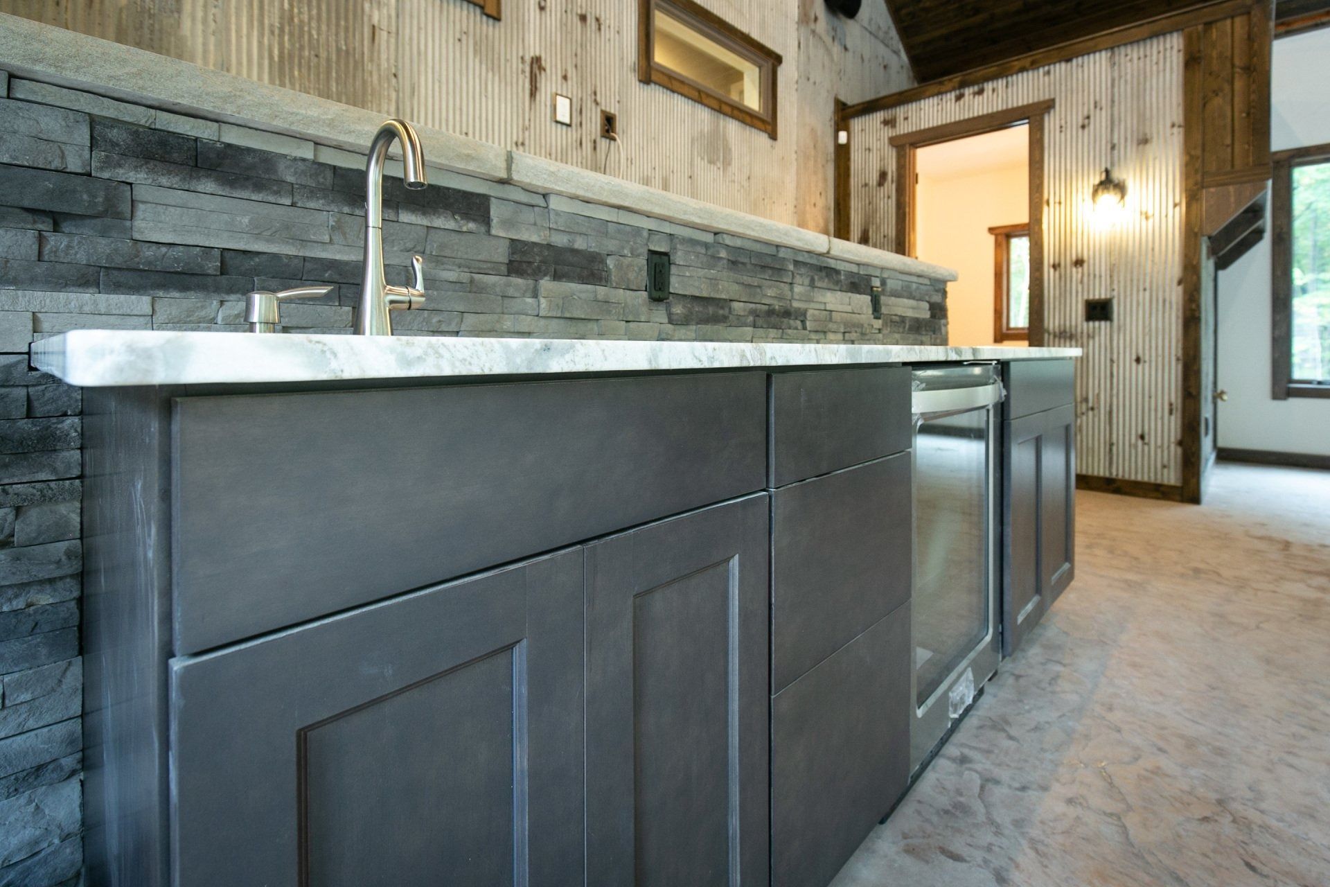 Bar with gray cabinets, stone backsplash, and wooden paneling in a rustic setting.