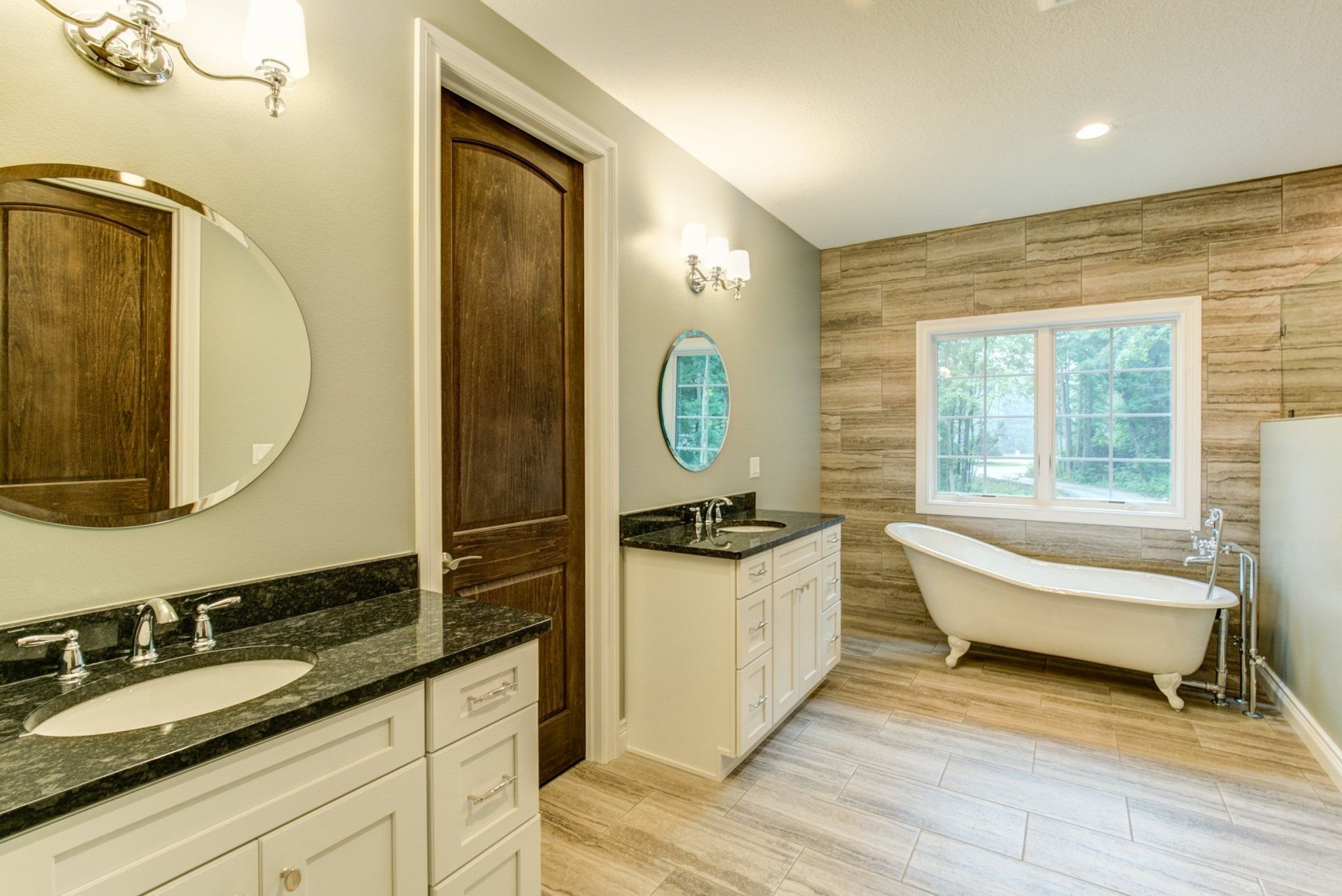 Bathroom with a clawfoot tub, two vanities, a dark wooden door, and a window.