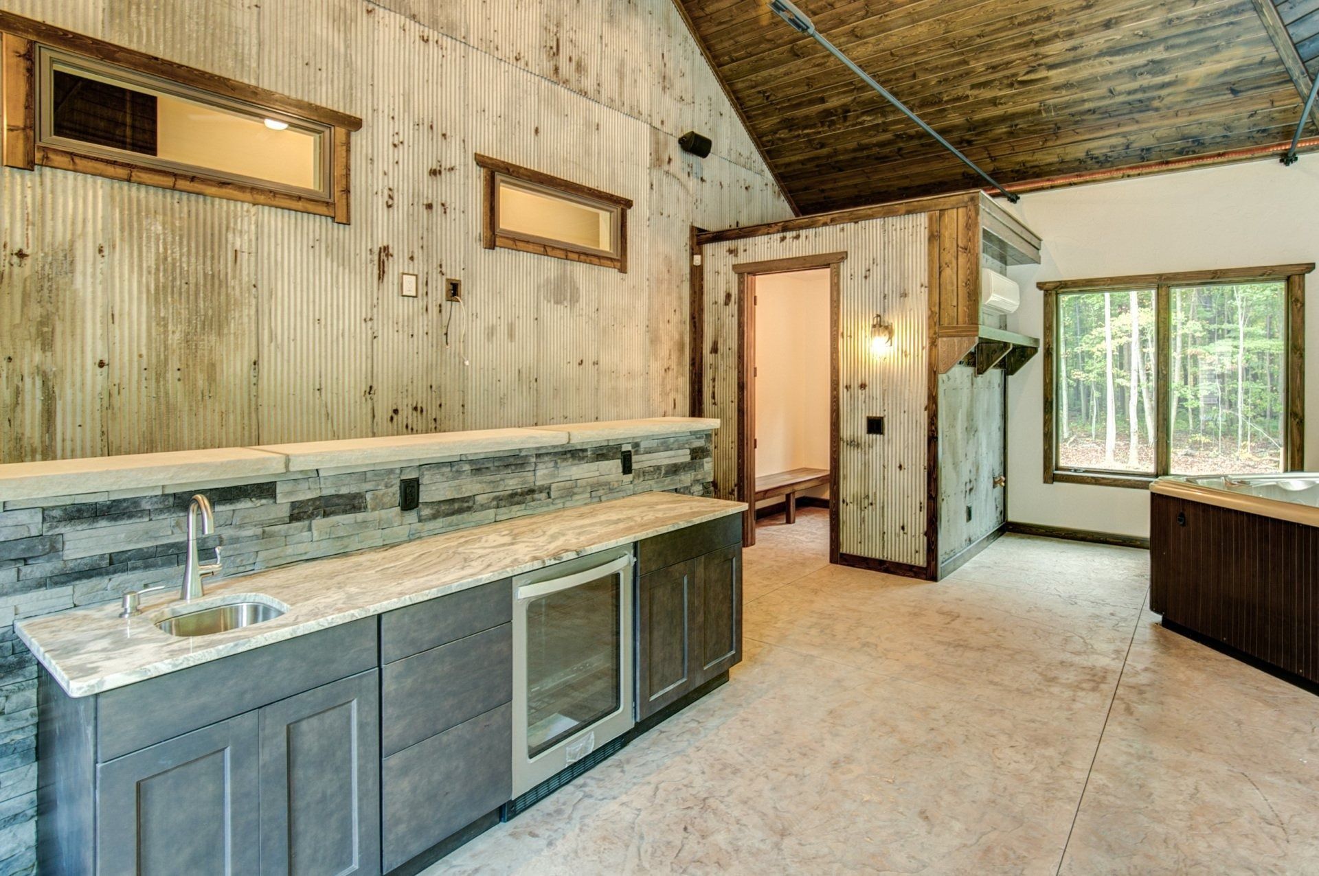 Interior bar area with corrugated metal walls, cabinetry, sink, and window overlooking trees.