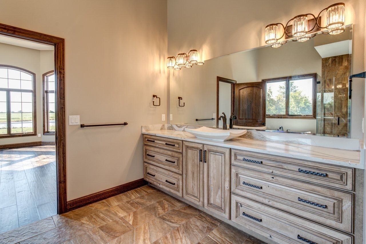Bathroom with light wood vanity, marble countertop, large mirror, and open doorway to another room.