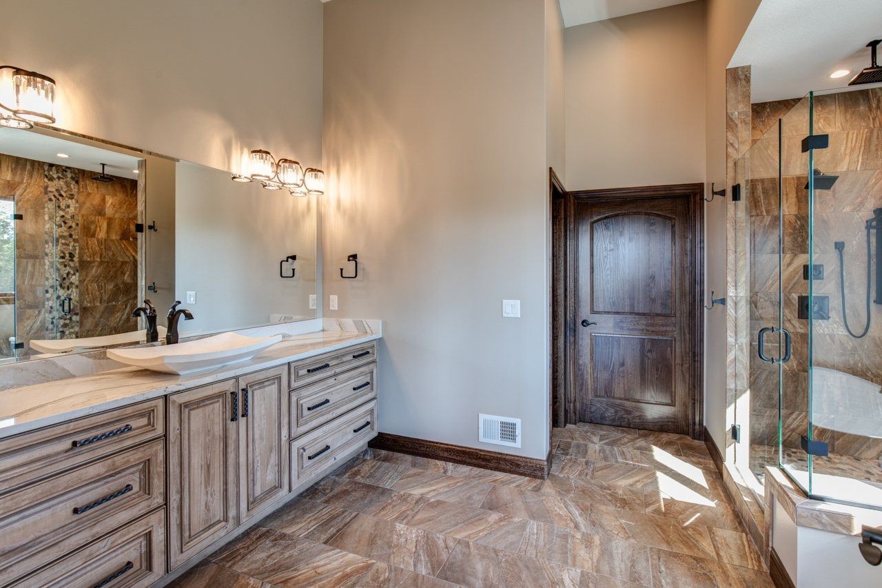 Bathroom with light wood cabinets, stone tile, glass shower, and brown door.