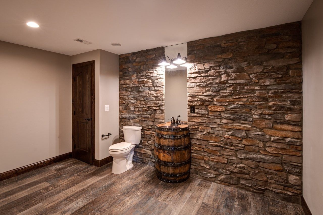 Rustic bathroom with stone accent wall, barrel sink, and wooden-look flooring.