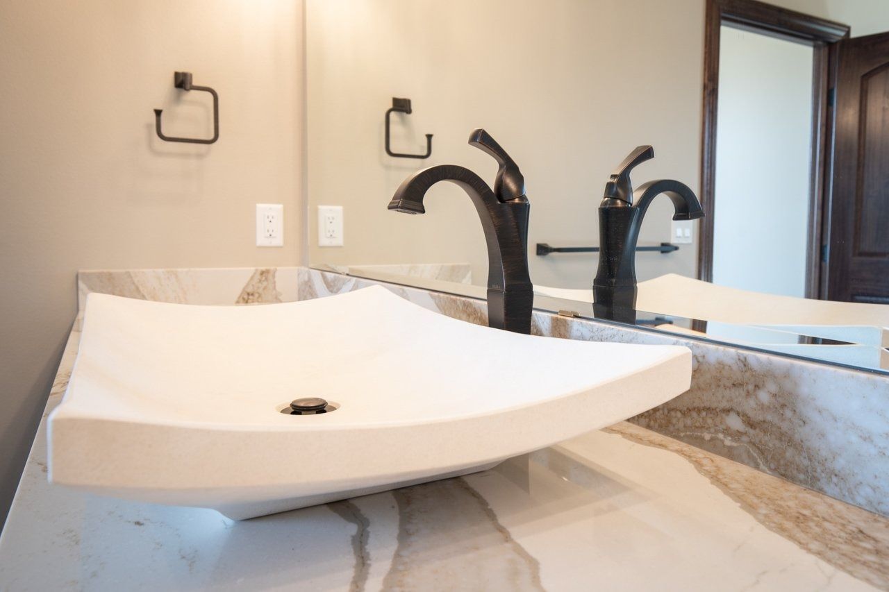 Bathroom with a white, modern vessel sink, bronze faucet, and marble countertop.