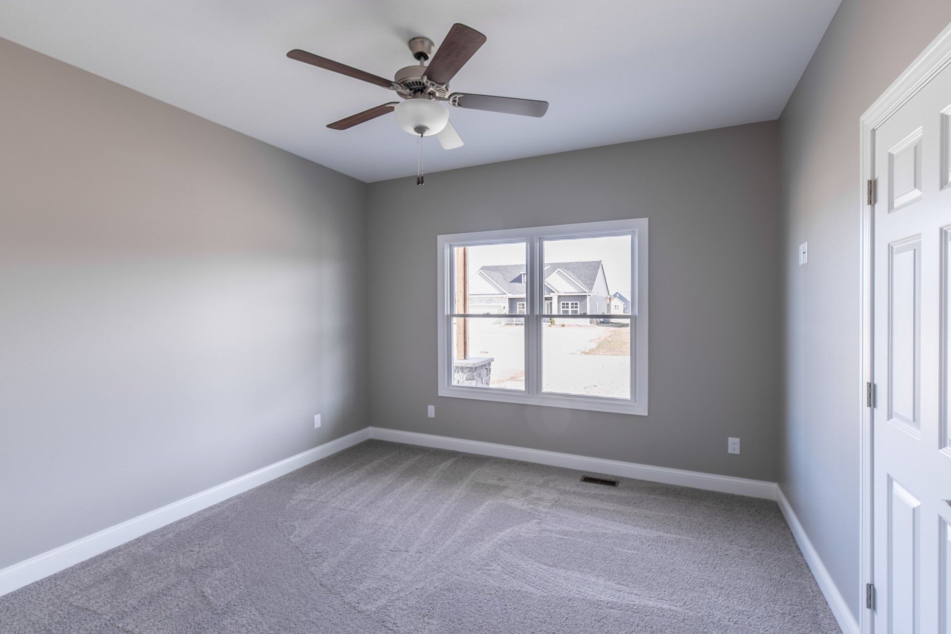 Empty bedroom with gray walls, carpet, and a ceiling fan, with a window and door.