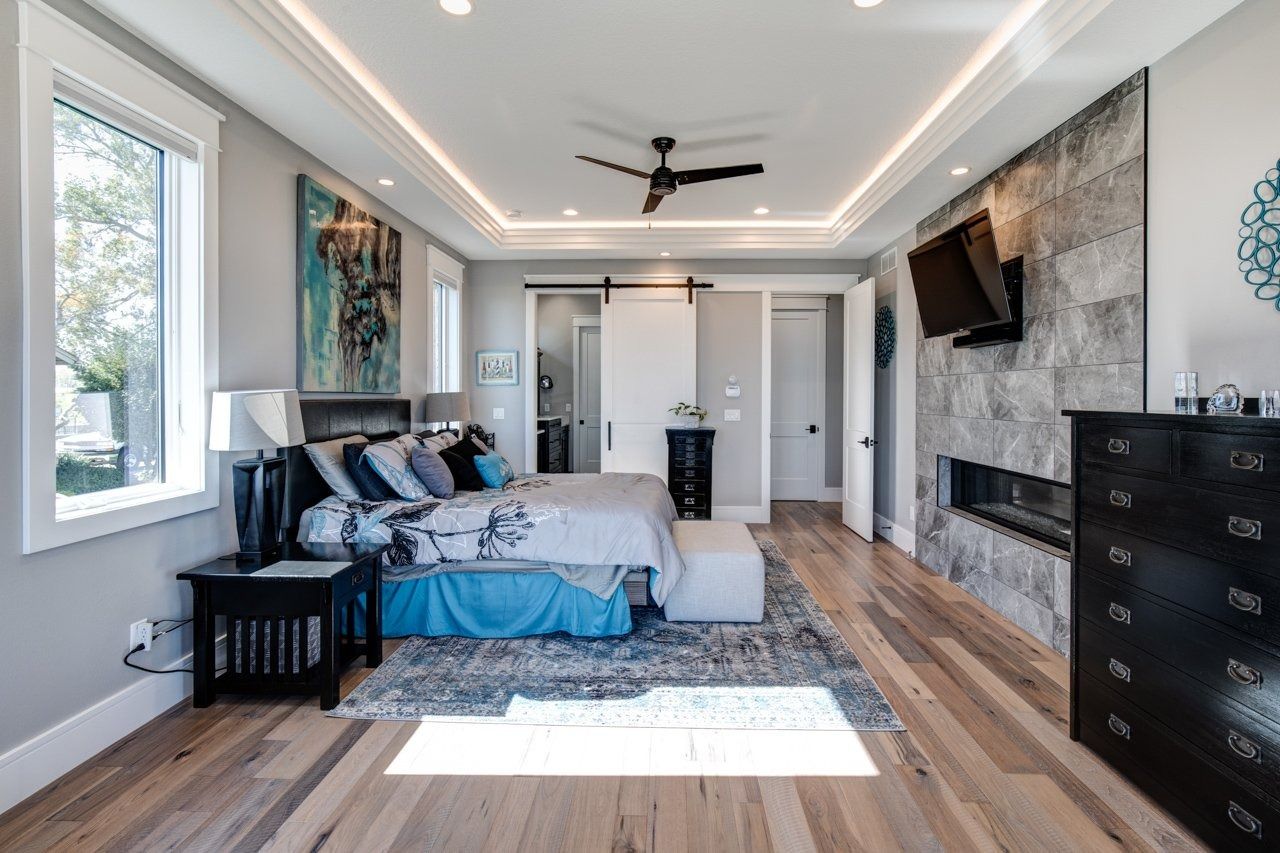 Luxurious bedroom with fireplace, TV, and king bed, light wood floors, gray walls, and blue accents.