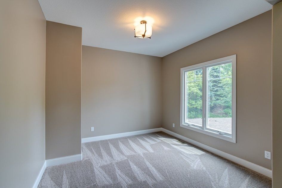 Empty room with tan walls, white trim, window, and patterned carpet.