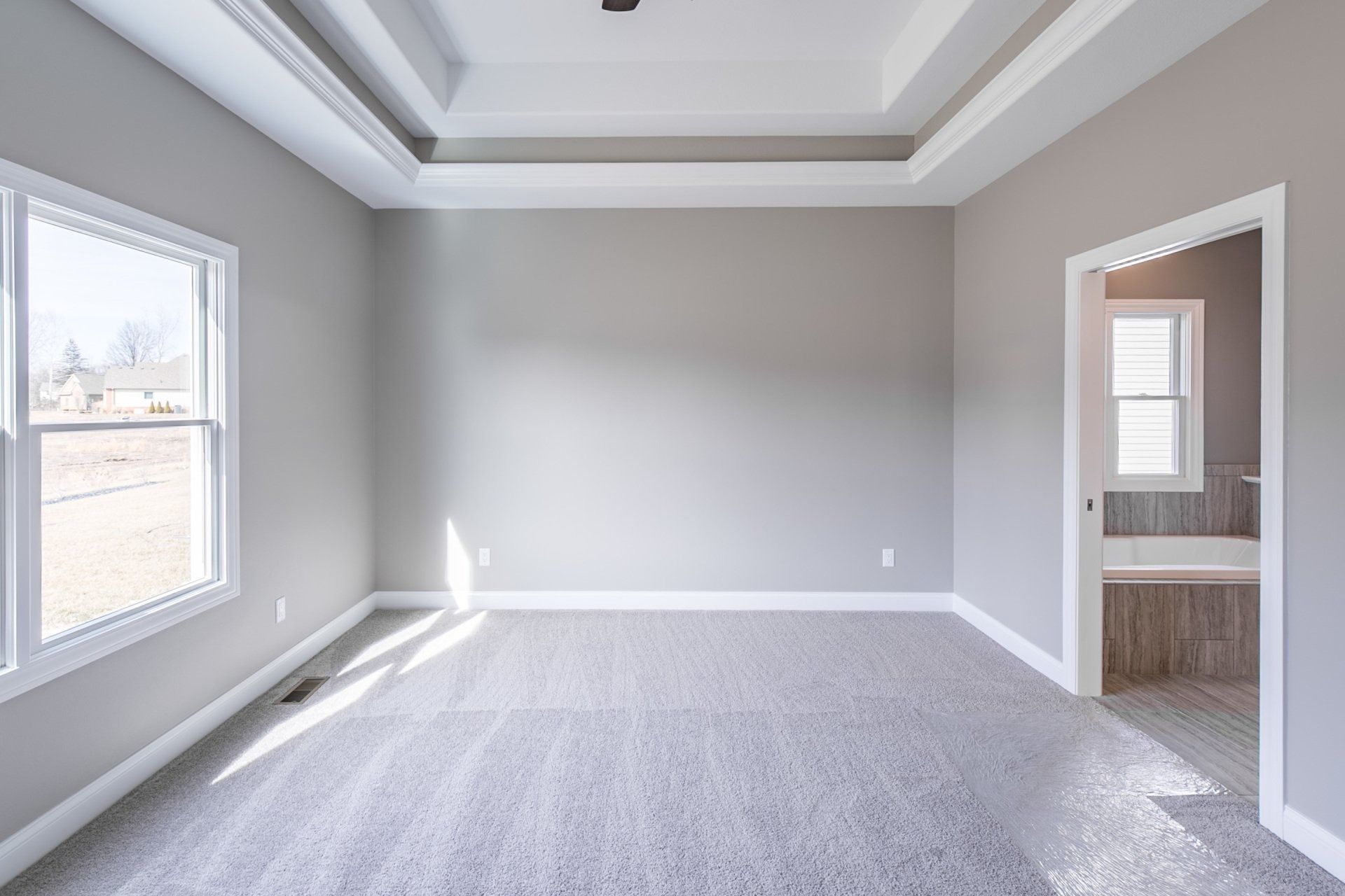 Empty bedroom with gray walls, white trim, carpet, and a view into a bathroom.