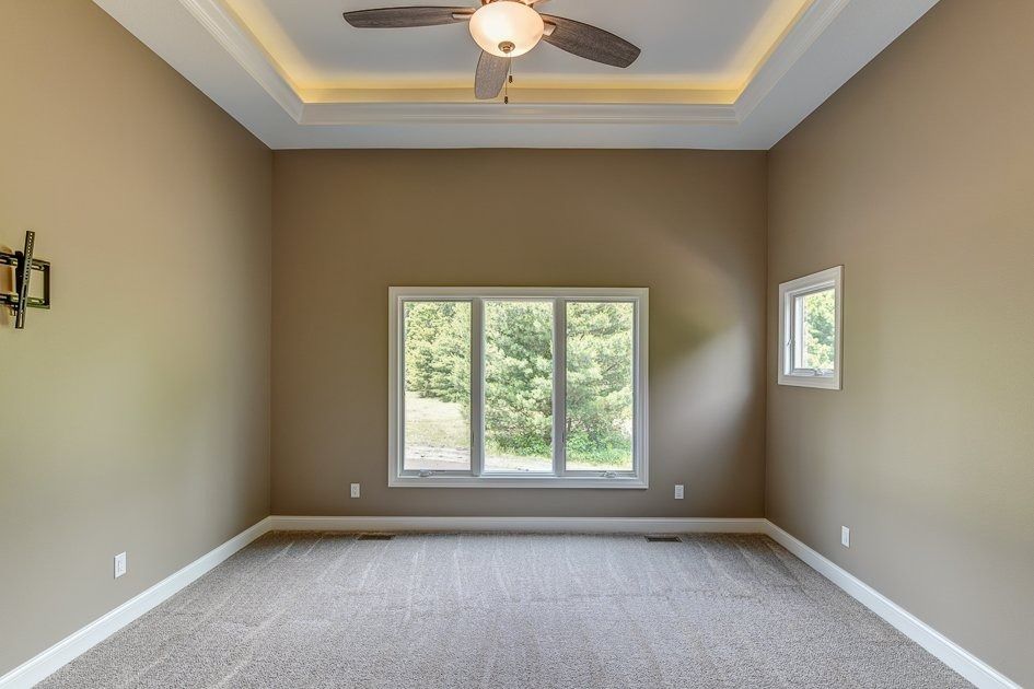 Empty beige-painted room with carpet, windows, ceiling fan, and trim.