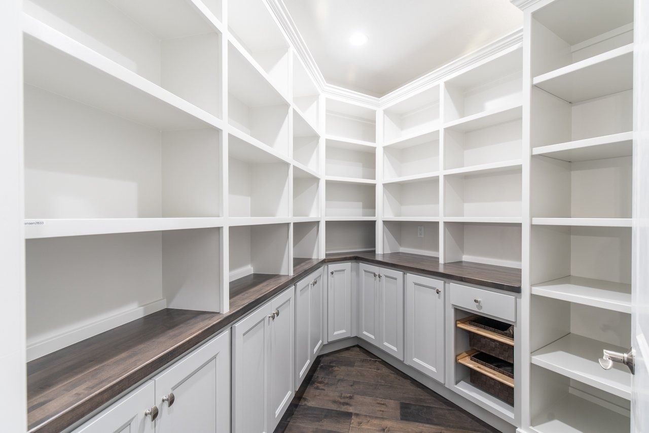 White pantry with built-in shelves and cabinets; dark countertops and wood flooring.