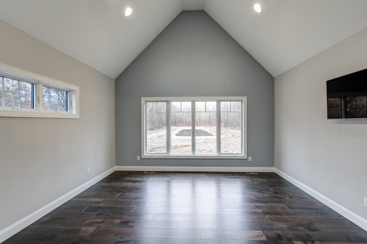 Empty room with vaulted ceiling, large windows, and dark wood flooring. Gray and white walls.