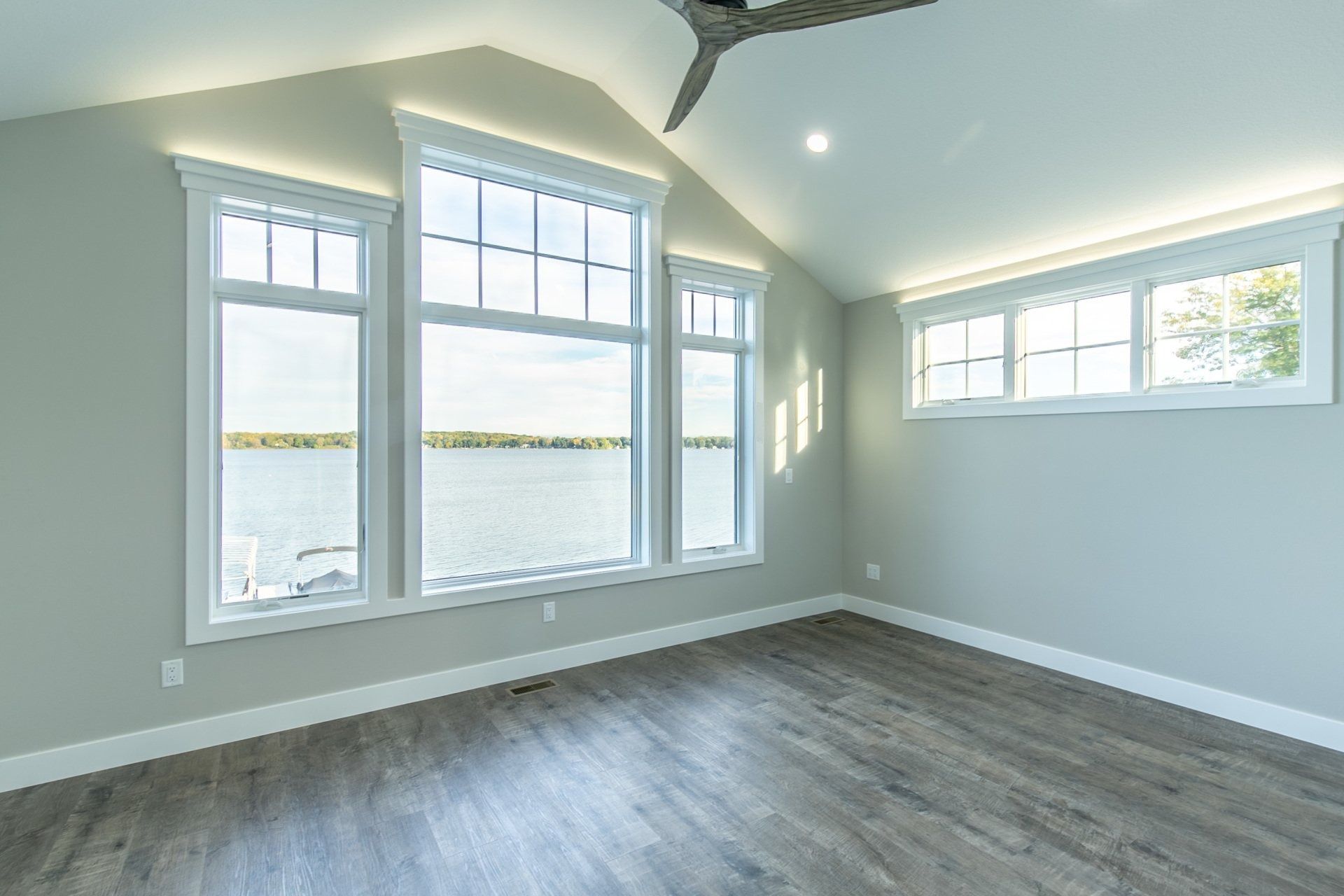 Empty room with large windows overlooking water, gray walls, and wood flooring.