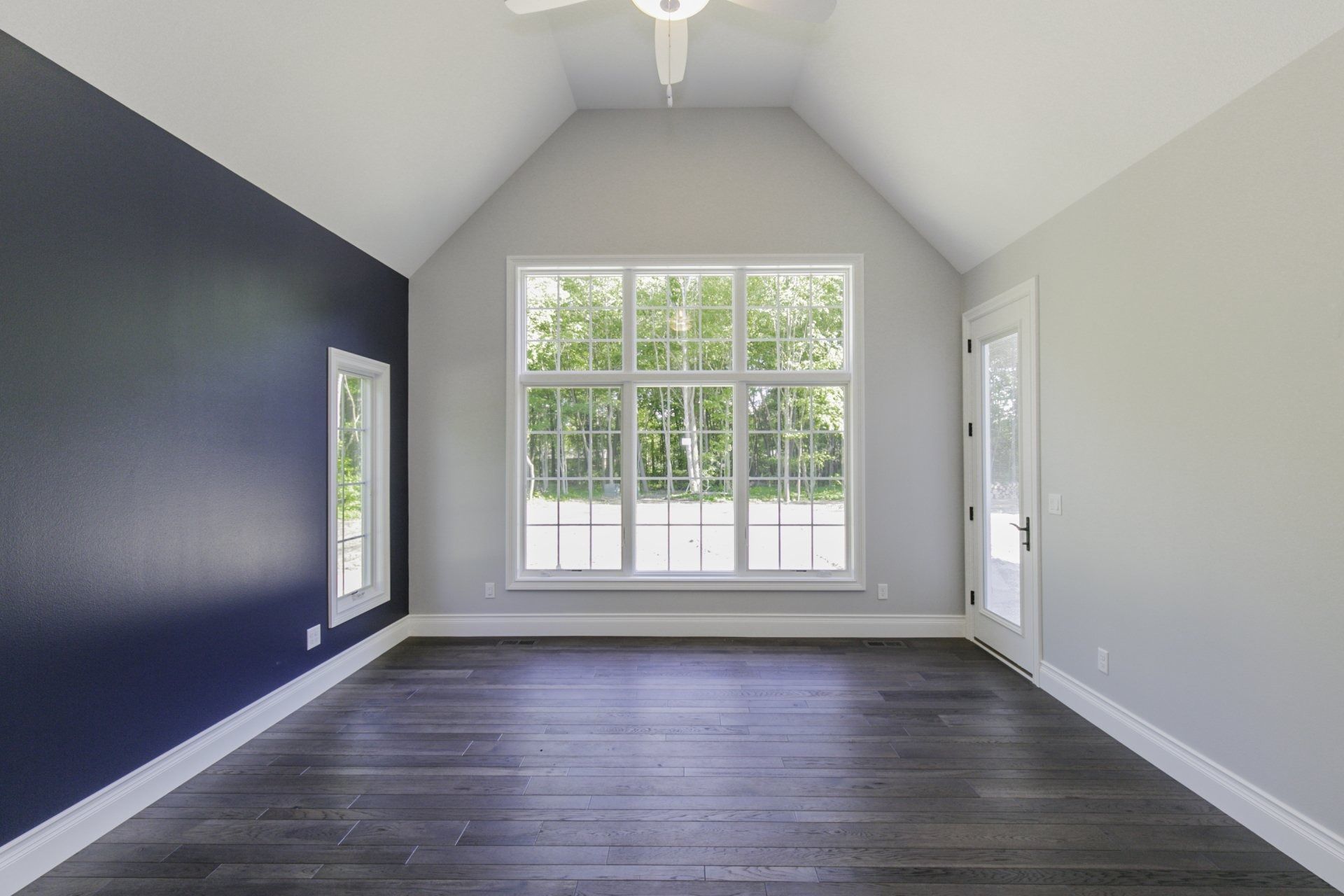 Empty room with dark hardwood floors, large windows, and a navy blue accent wall.