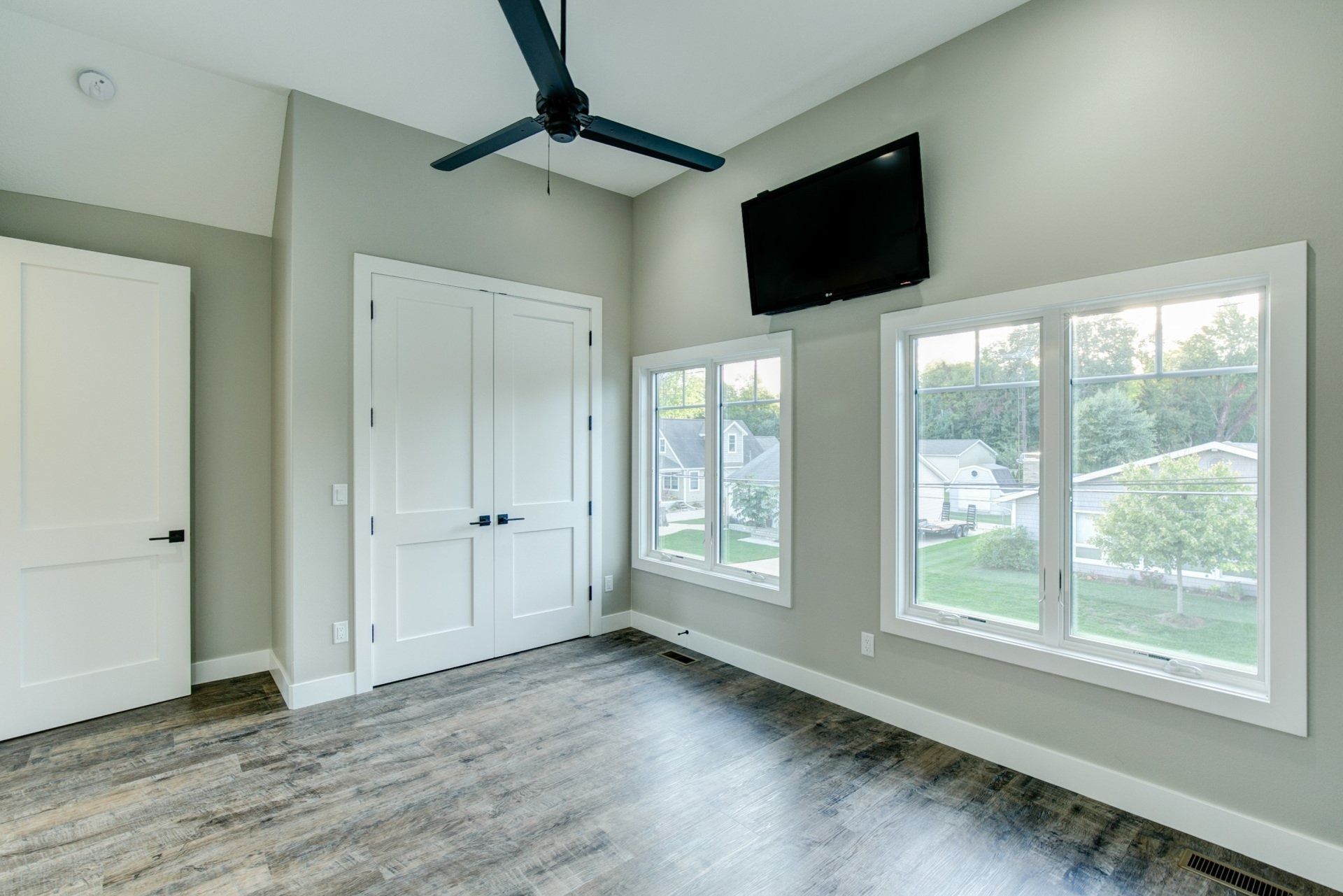 Empty bedroom with gray walls, two windows, and a mounted TV.