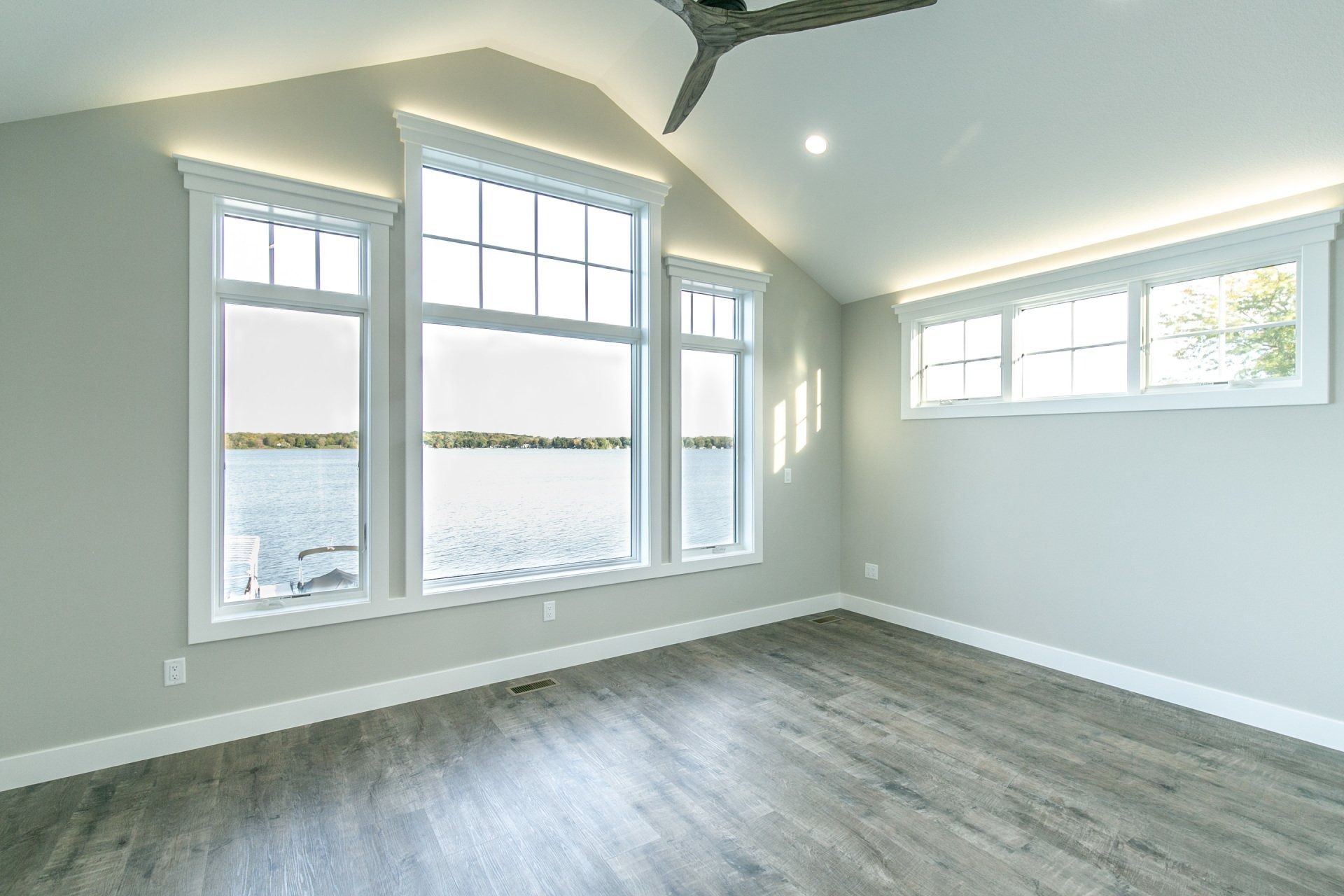 Bright bedroom with large windows overlooking water, gray walls, and wood-look flooring.