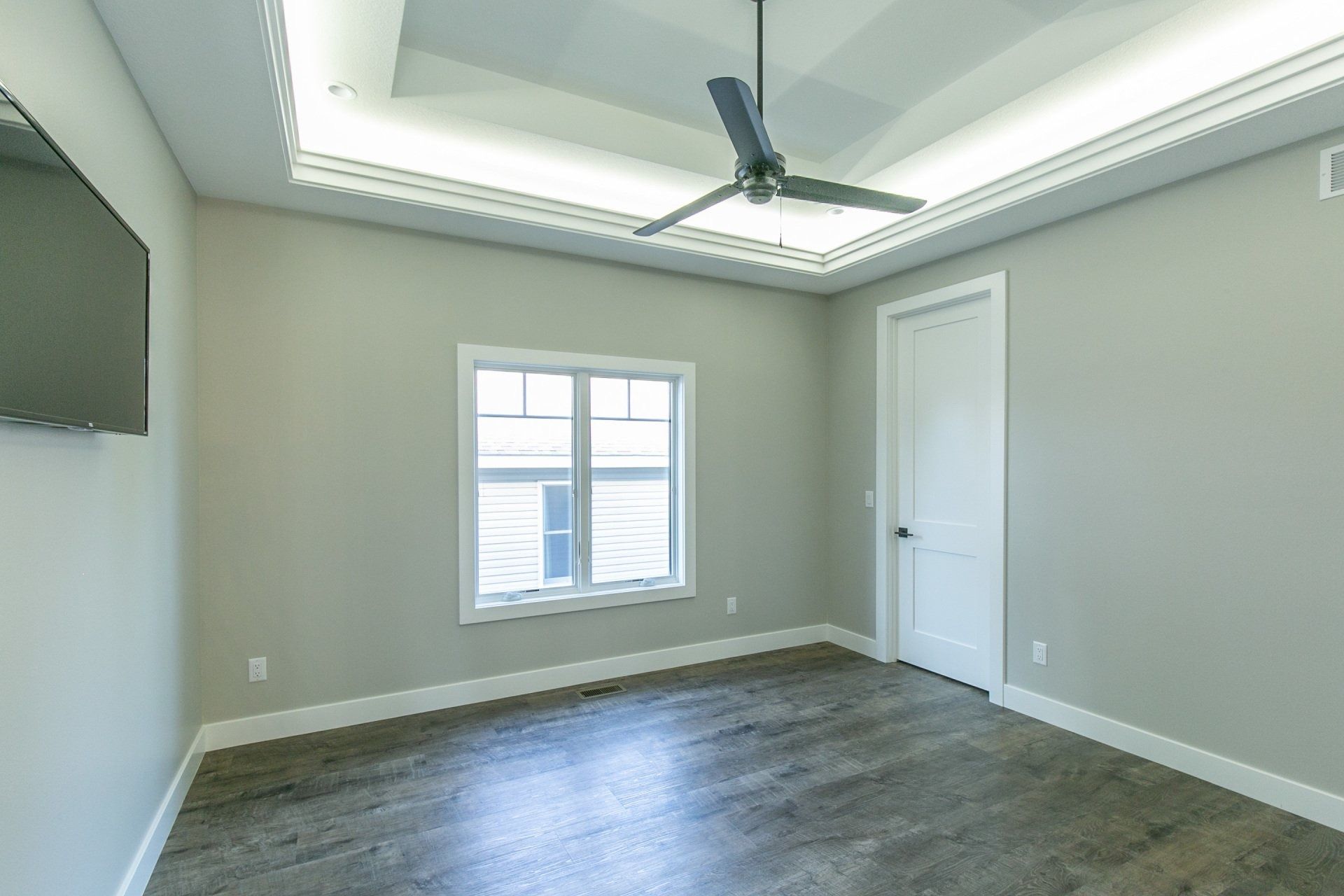 Empty room with gray walls, wood-look flooring, white door, window, and ceiling fan.