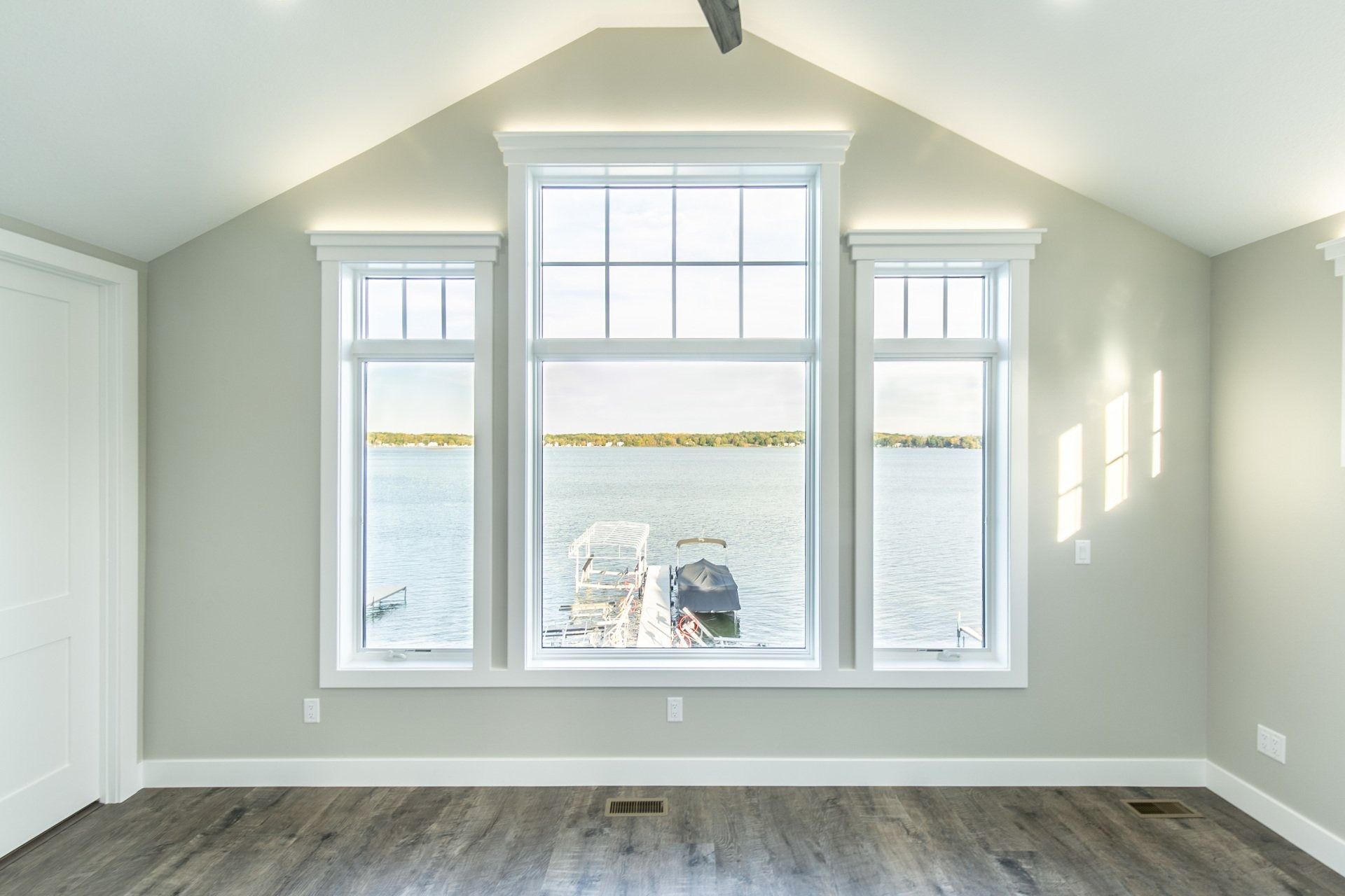 Empty room with three windows overlooking a body of water and a dock.