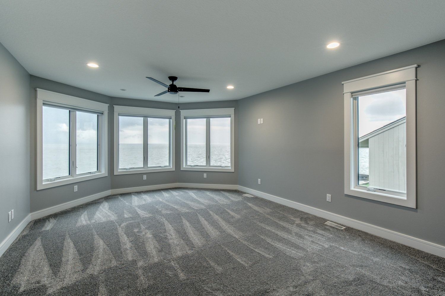 Gray-walled bedroom with large windows, dark carpet, and a ceiling fan.