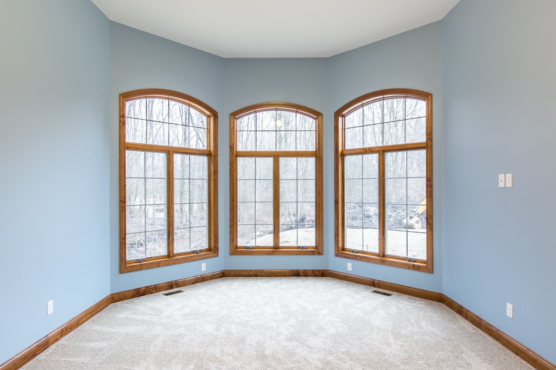 Empty room with three arched windows framed in brown, light blue walls, and beige carpet.