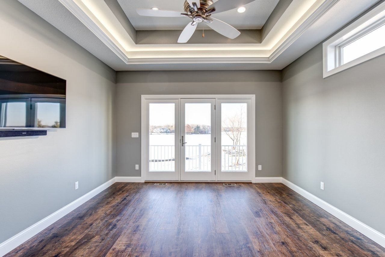 Empty gray room with dark wood floor, white doors to a balcony, and a coffered ceiling.