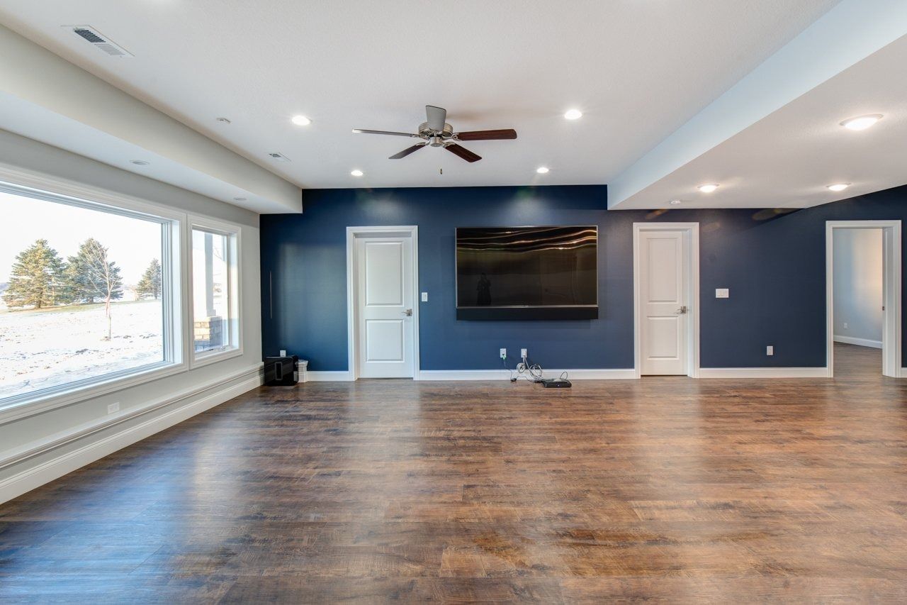 Spacious, empty room with hardwood floors, navy blue accent wall with mounted TV, and large windows.