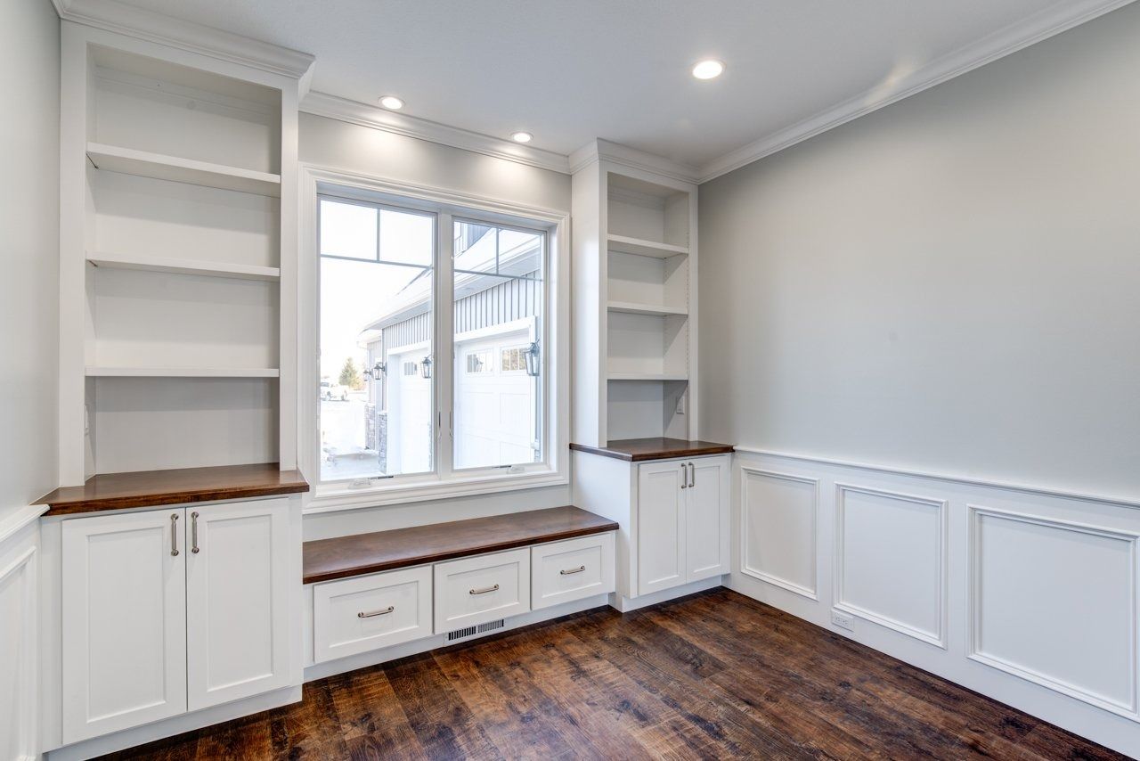 A window seat with built-in bookshelves and storage cabinets in a room with hardwood floors and light gray walls.
