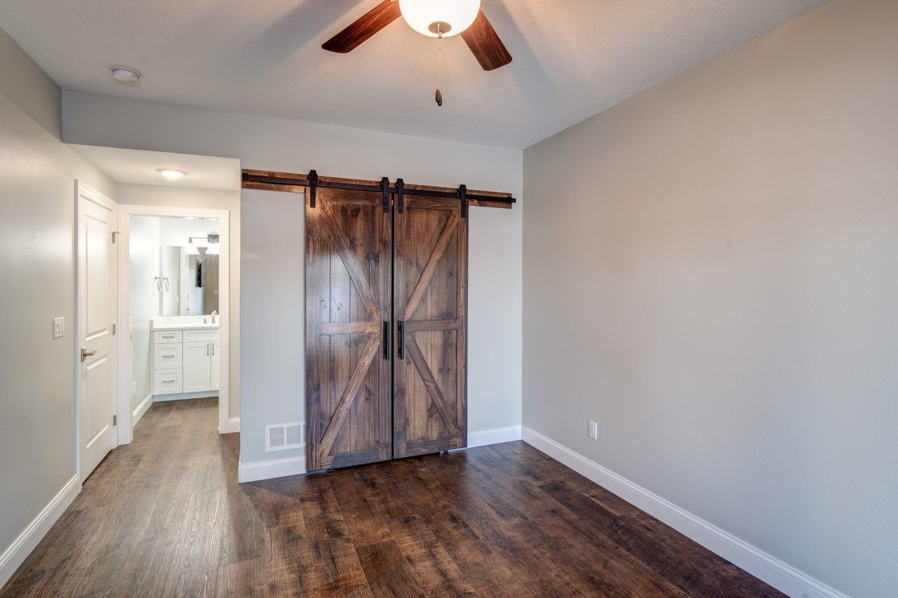 Bedroom with wood floors, barn doors, and a doorway to a white bathroom with a vanity.