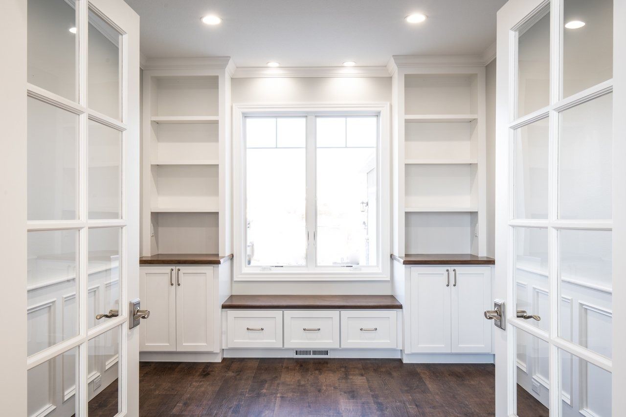 White built-in bookshelves and cabinets flank a window with a dark bench. French doors open to the room.
